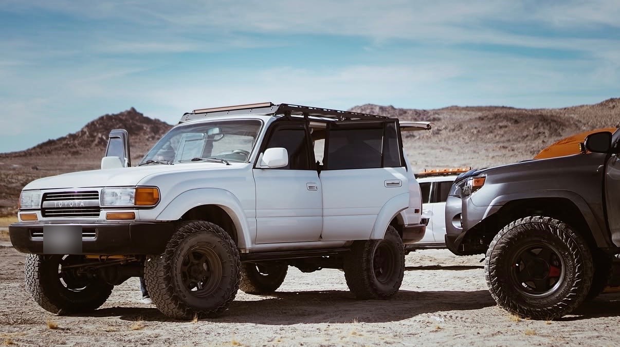 Lifted white Toyota Land Cruiser and a grey 4Runner parked in the desert